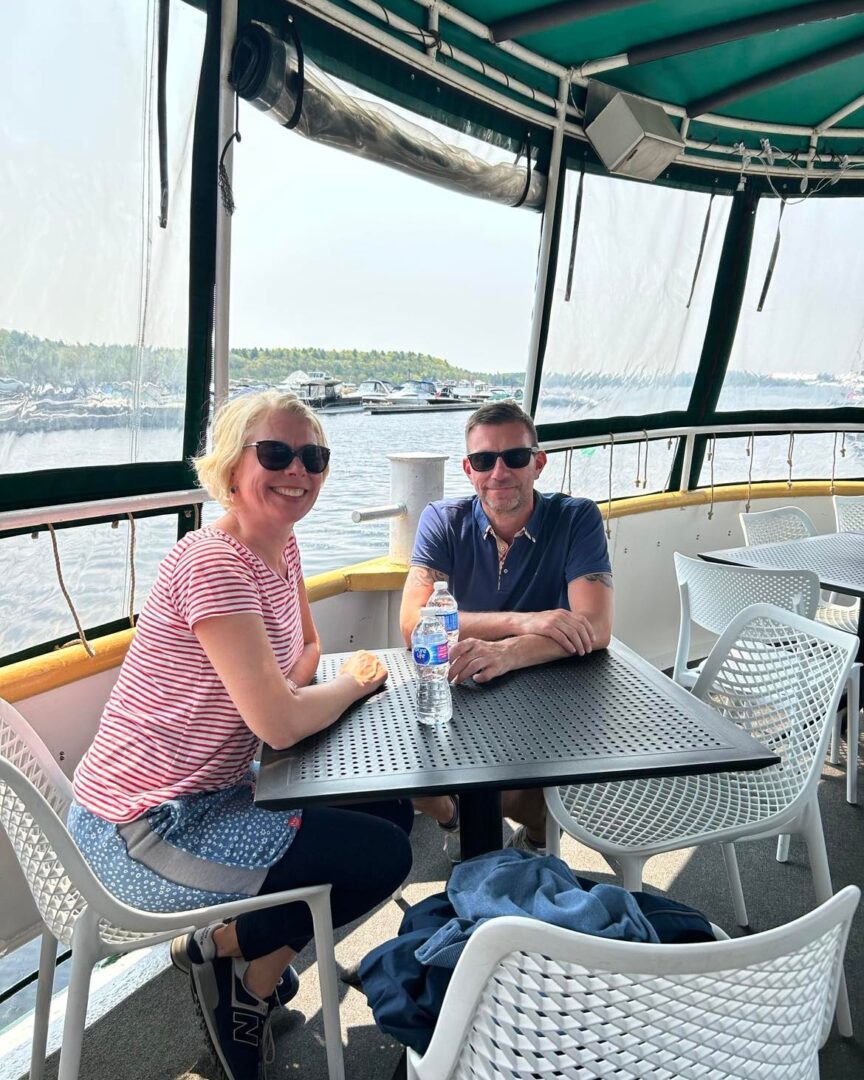 A man and woman sitting at a table on the deck of a boat.